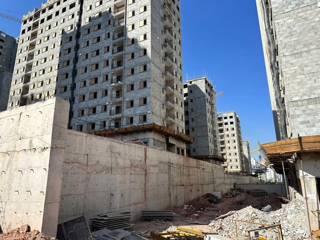 Parede de contenção em concreto com edifícios ao fundo em obra de fundações e contenções