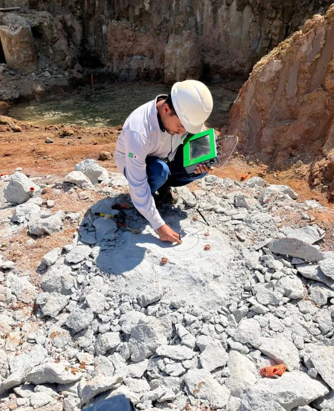 Técnico realizando ensaio PIT Pile Integrity Test em rocha com equipamento portátil em escavação