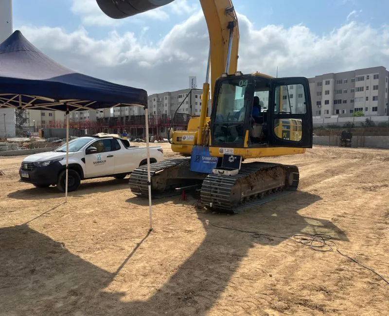 Escavadeira amarela com tenda e pickup Sammour em canteiro de obras urbano