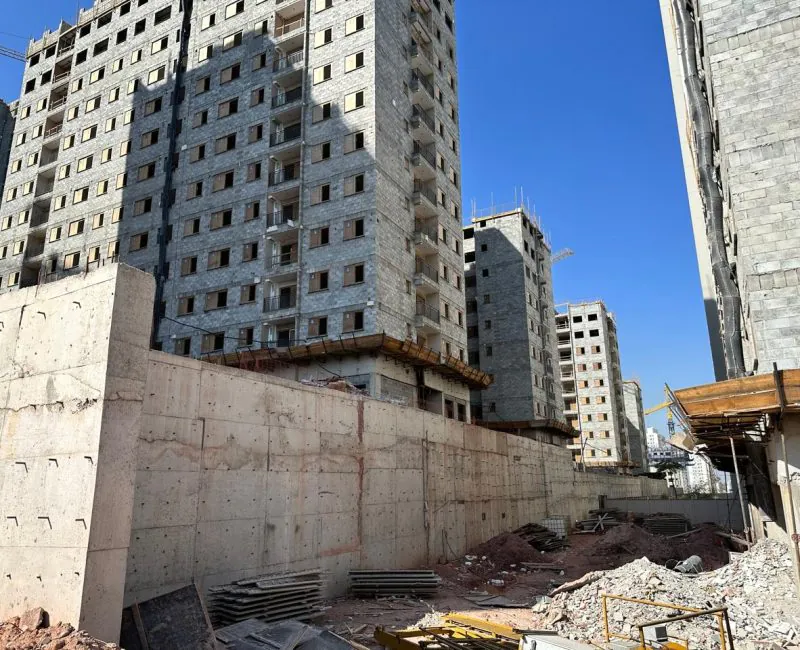 Parede de contenção em concreto com edifícios ao fundo em obra de fundações e contenções