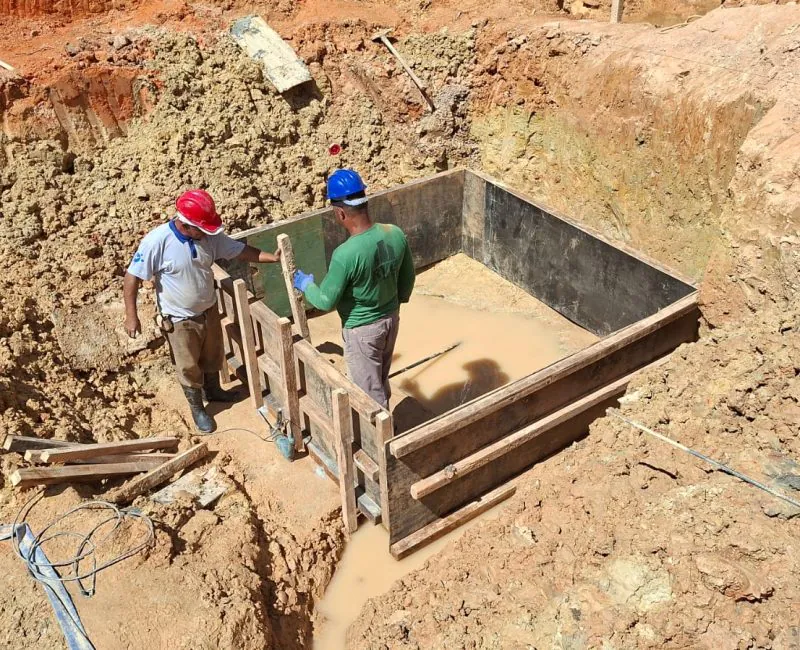 Trabalhadores instalando fôrmas de madeira em vala de escavação para fundação